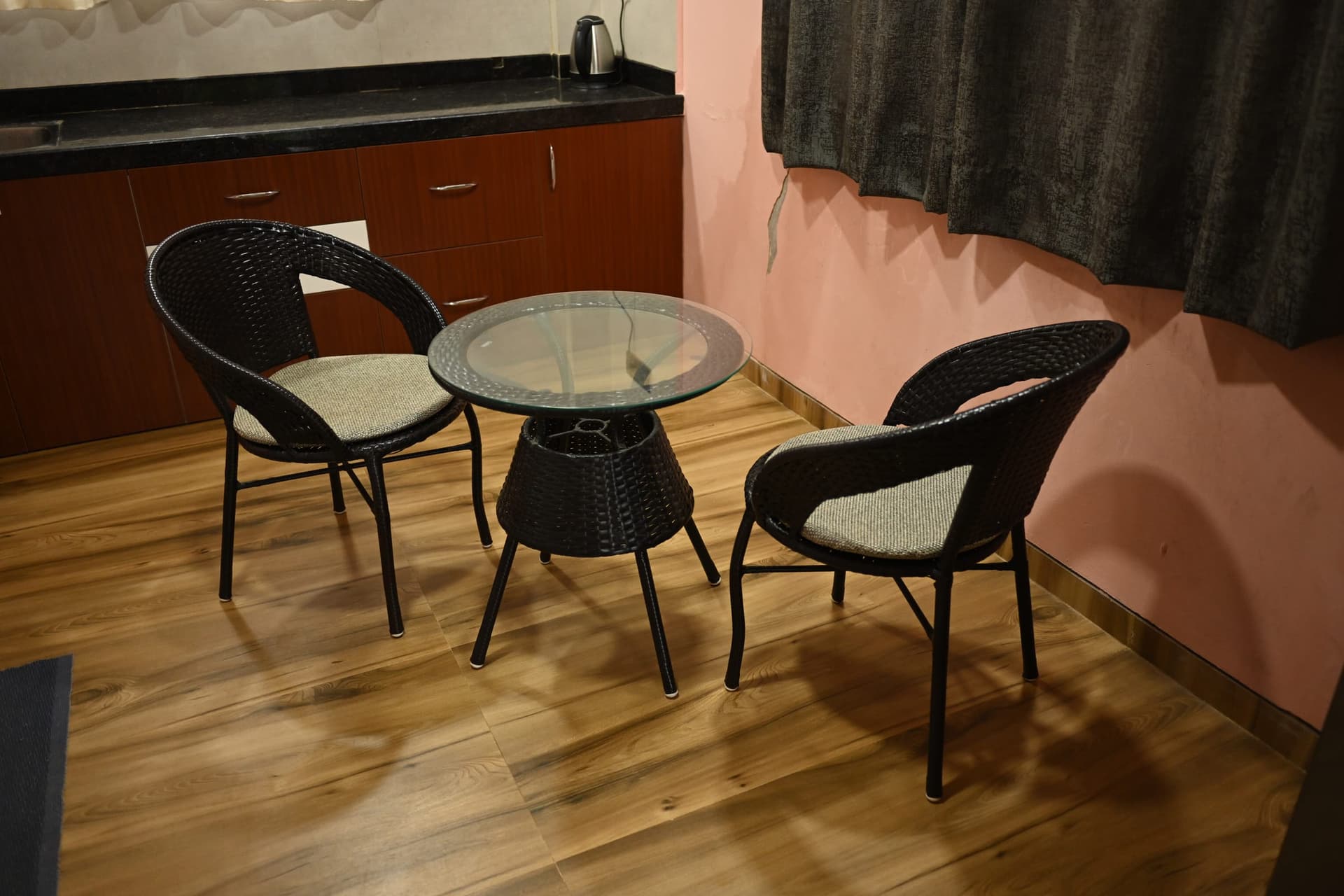 The dining corner of a suite — glass table and two woven chairs beside the kitchenette