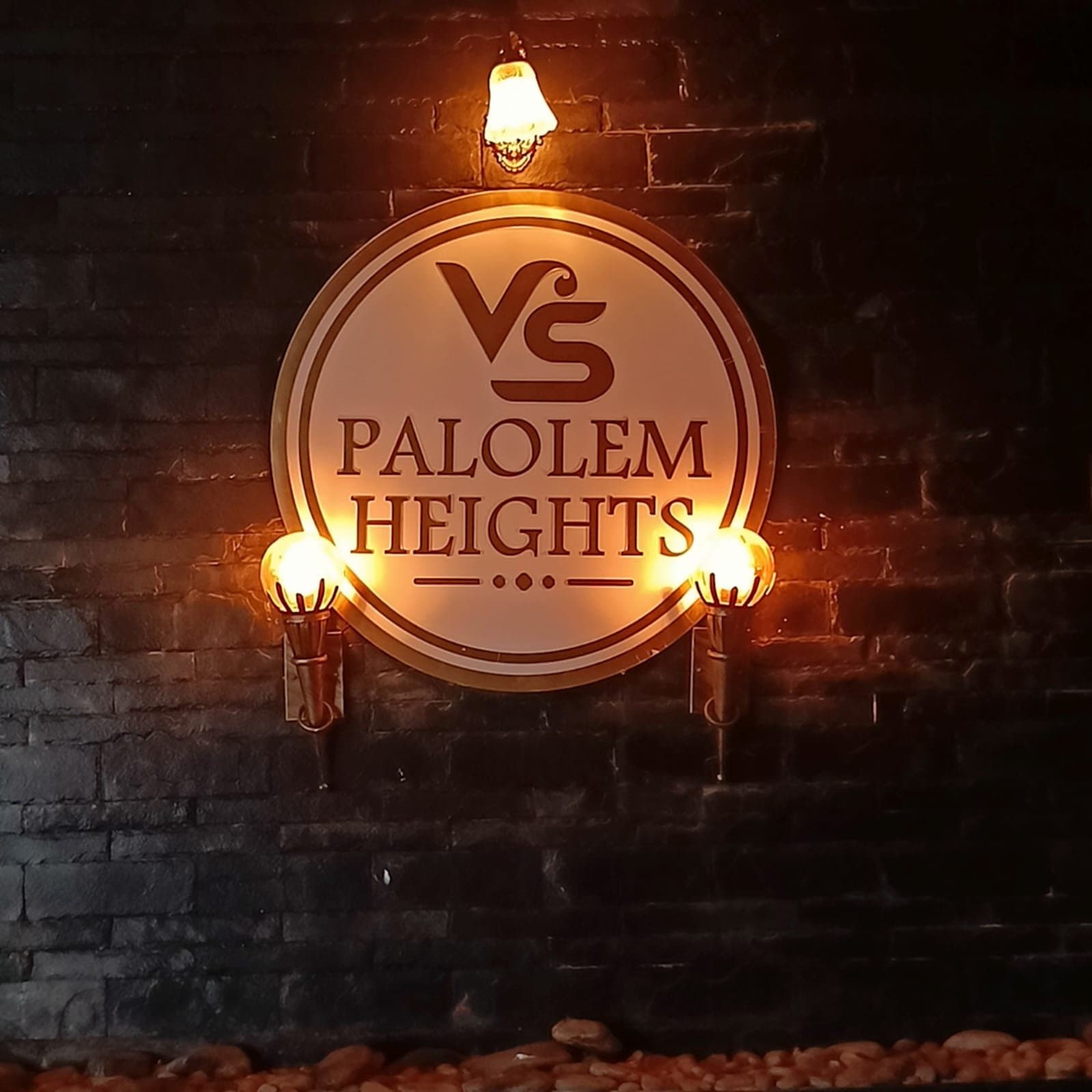 The Palolem Heights sign in lamplight on the stone wall by the pool